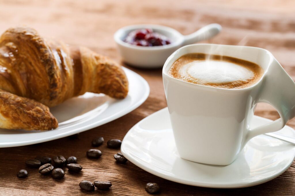 Extreme close up of Creamy coffee on wooden table with croissant in background.
