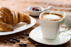 Extreme close up of Creamy coffee on wooden table with croissant in background.